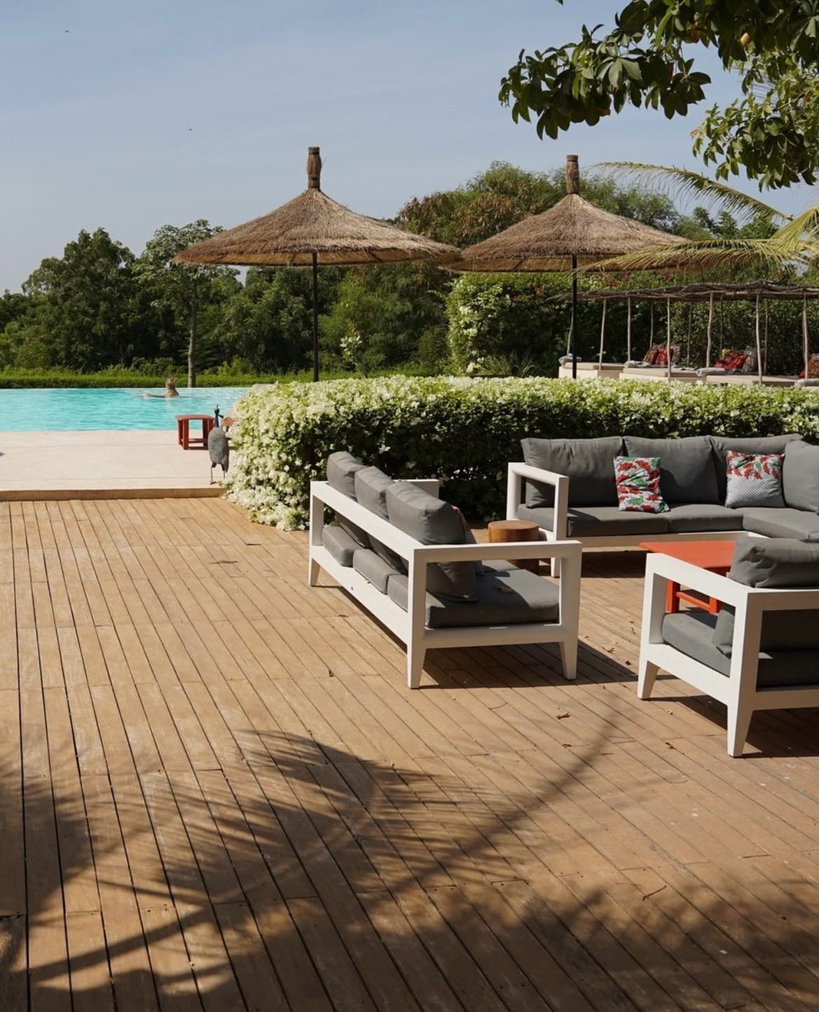 Terrasse en bois et salon extérieur face à la piscine, sous des parasols en paille