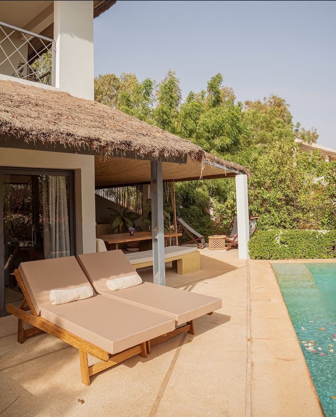 Terrasse d'un bungalow à toit de paille, transats le long de la piscine