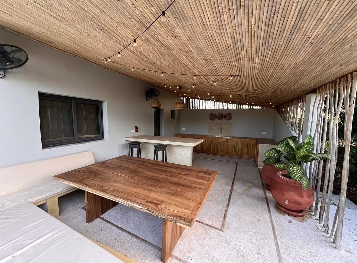 Espace commun : grande table en bois massif sous un plafond en canisse