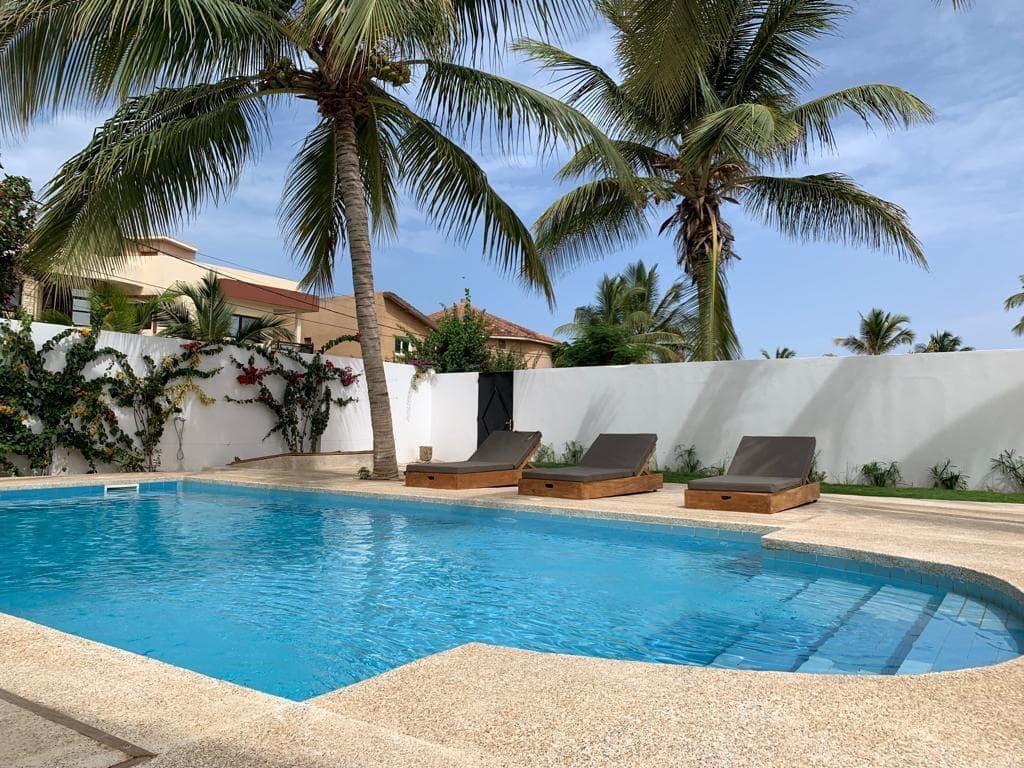 Piscine aux formes arrondies bordée de transats, palmiers et mur d'enceinte blanc